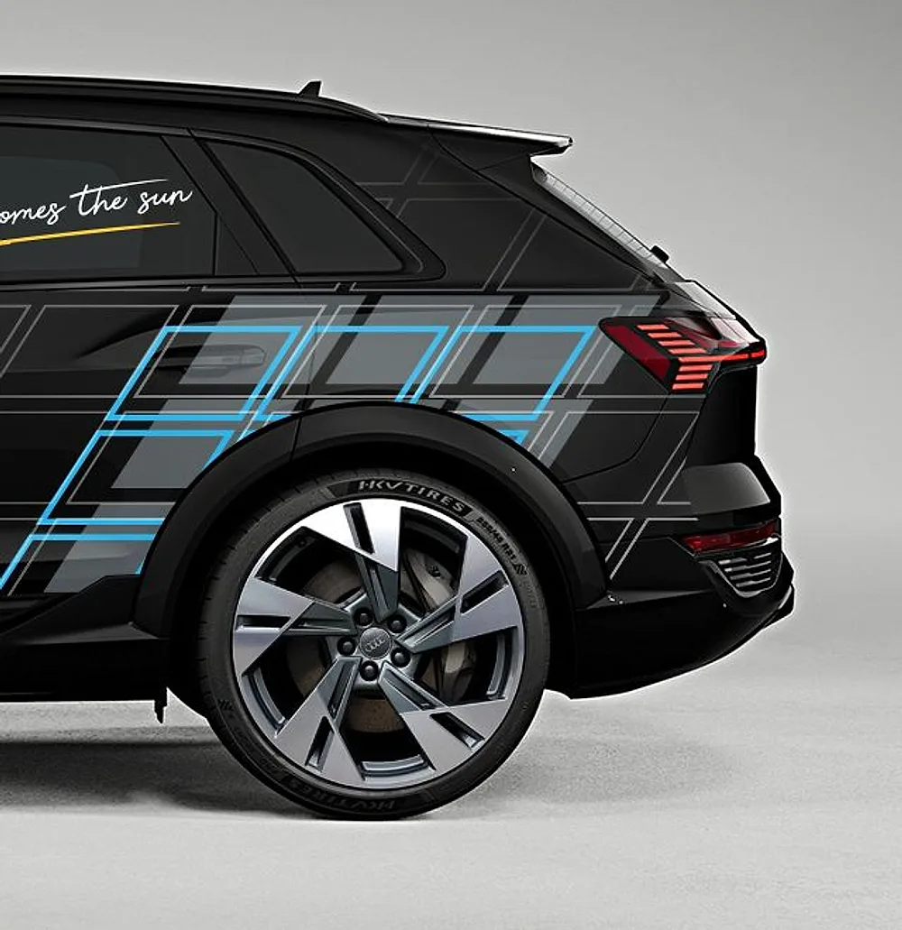 Heck eines schwarzen SUV mit Fahrzeugdesign von Elite PV: Modulmuster in Blau und Grau, Schriftzug „Here comes the sun“